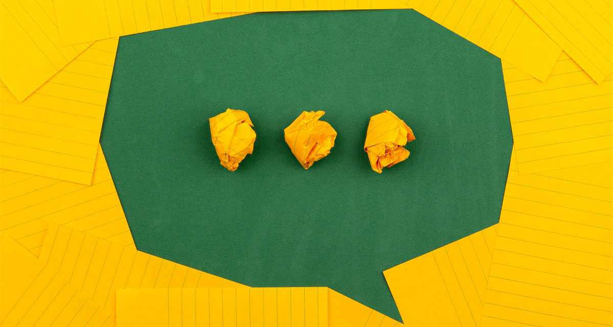 3 zerknüllte gelbe Papierkugeln auf grüner Sprechblase, umgeben von gelb linierten Papieren. / Quelle: Foto: unsplash.com | Volodymyr Hryshchenko 3 zerknüllte gelbe Papierkugeln auf grüner Sprechblase, umgeben von gelb linierten Papieren.